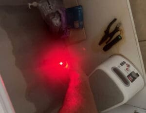 Moisture detection tool emitting a red light, inspecting water damage under a sink with visible damp areas.