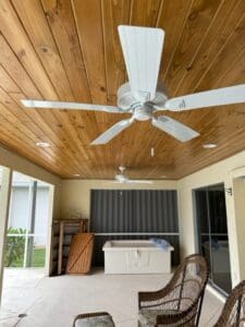 Outdoor patio with wooden ceiling and white ceiling fans installed, showcasing a completed renovation project.